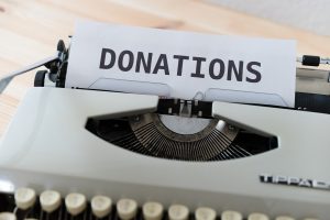 Typewriter with a piece of paper emerging and the word DONATIONS written in text that is surely larger than the keys would actually permit