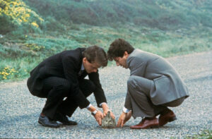 Two men are crouching on a tarmac road.